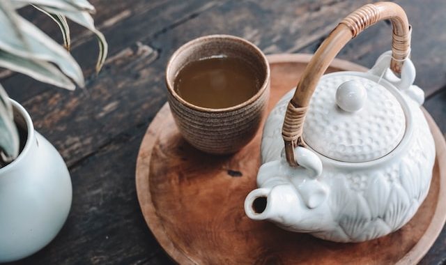 konvice a šálek s čajem aranžované na dřevěném tácku